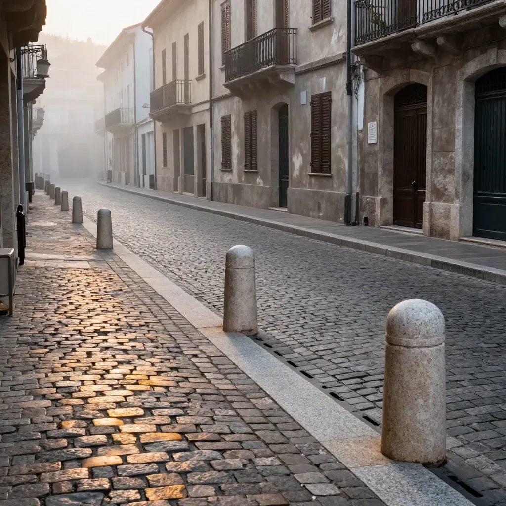 Strada storica in ciottoli con cordoli in pietra e stalli ordinati, luce ambra nella nebbia.